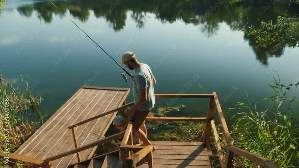 Dad and his little son with fishing rods in their hands go down the steps to a wooden pier to fish on the lake Dad and his little son with fishing rods in their hands go down the steps to a wooden pier to fish on the lake