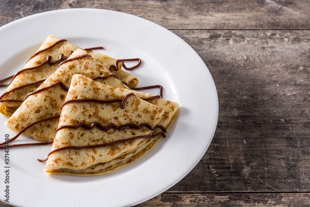 Sweet crepes with chocolate syrup on wooden table. Copy space