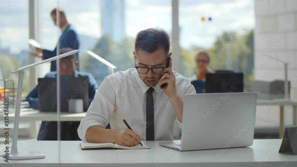 Portrait of young entrepreneur in open space office making phone call and writing down information Portrait of young entrepreneur in open space office making phone call and writing down information