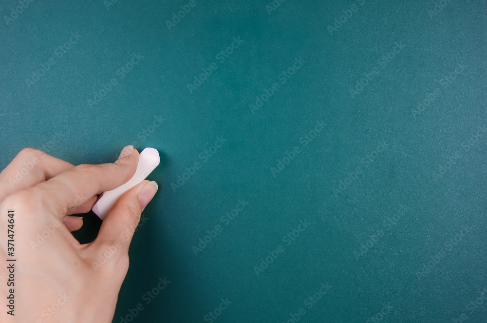 Naklejka premium woman's left hand holds a white chalk and is about to write on a green Board, copying space.