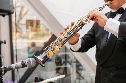 A musician at the event in a frock coat and bow tie plays the saxophone. Сlose-up of hands and tools