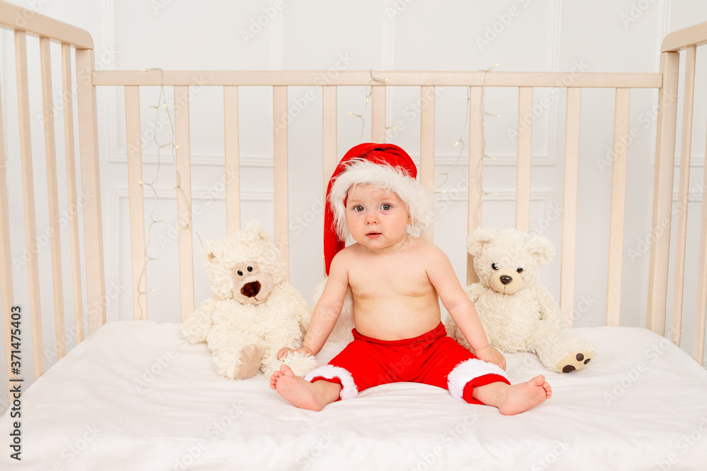 Obraz premium a small child is lying in a crib in a Santa hat with stuffed toys bears, happy new year 2021, space for text