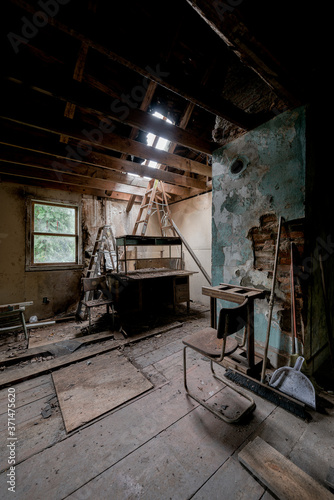 Inside a derelict attic with sketchy stacked furniture below a hole in the roof at a long-abandoned house in New York.