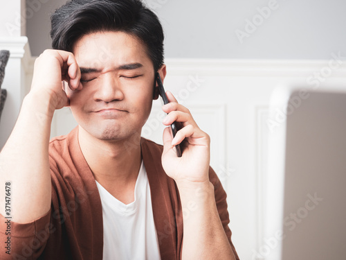 Asian young man rubbing his tired eyes his smartphone.