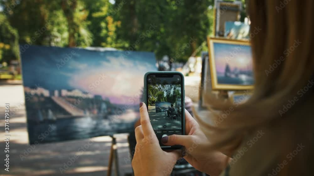 Unknown woman taking photos on smartphone of man artist who drawing a picture