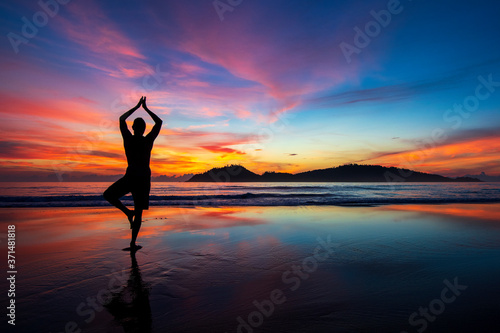 A man is doing a yoga pose during a colorful sunrise at Campeche beach in Florianopolis Brazil