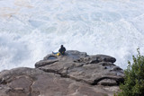 A person sitting on the rock and watching how storm waves crashing on the rocks