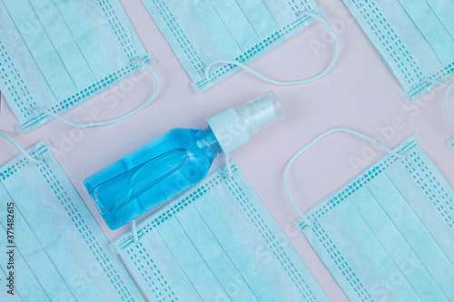 A closeup shot of a hand sanitizer and protective face masks on a pink background