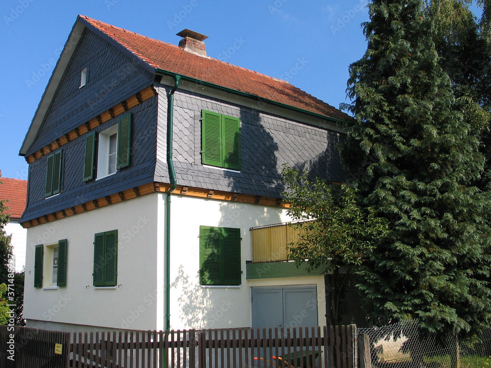 Altbau mit Spitzgiebel und Schieferverkleidung im hessischen Hinterland vor blauem Himmel.