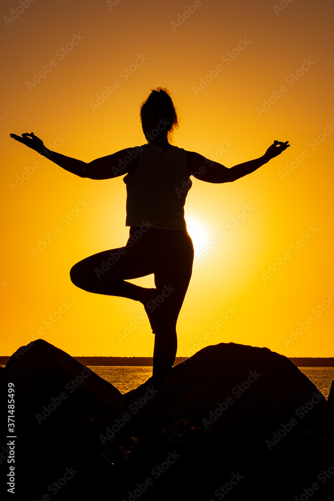 A young woman is keeping her balance during a Yoga pose in the sunset
