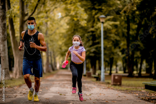 Fototapeta Naklejka Na Ścianę i Meble -  Young sporty man and girl are running in the park. They are wearing a protective face mask