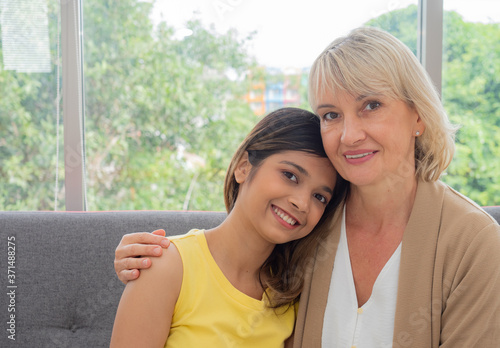 Obraz na plátně The adopted caucasian mother and Asian teen daughter happily hugged and smiled on the sofa