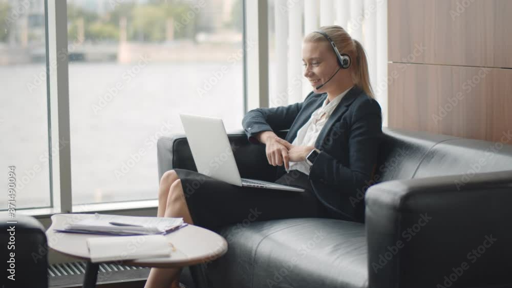 Portrait smiling young businesswoman in headset having video call working in lounge zone in office Portrait smiling young businesswoman in headset having video call working in lounge zone in office