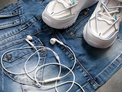 Fashionable outfit for girls. Minimal creative set. Fashionable white sneakers, trendy denim skirt, white headphones for the smartphone. urban youth style