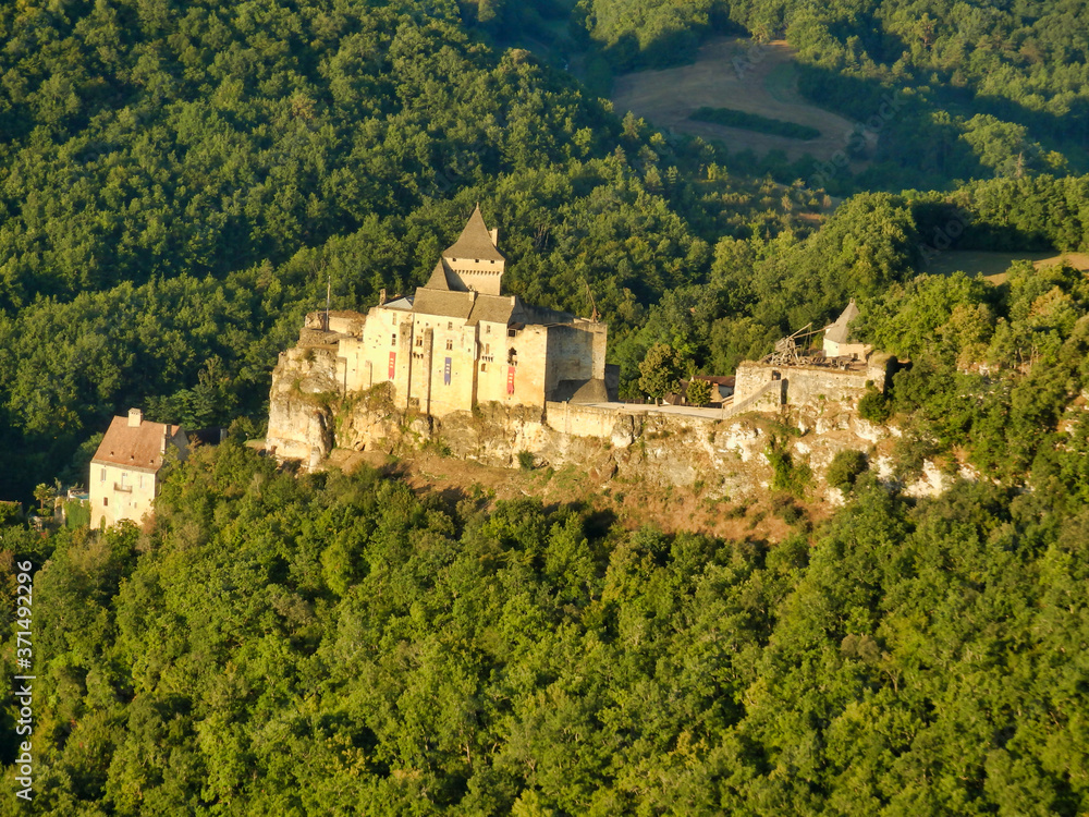 Aerial view of Chateau de Castelnaud in the Dordogne, France bathed in a golden glow at sunrise. Photo taken from a hot air balloon