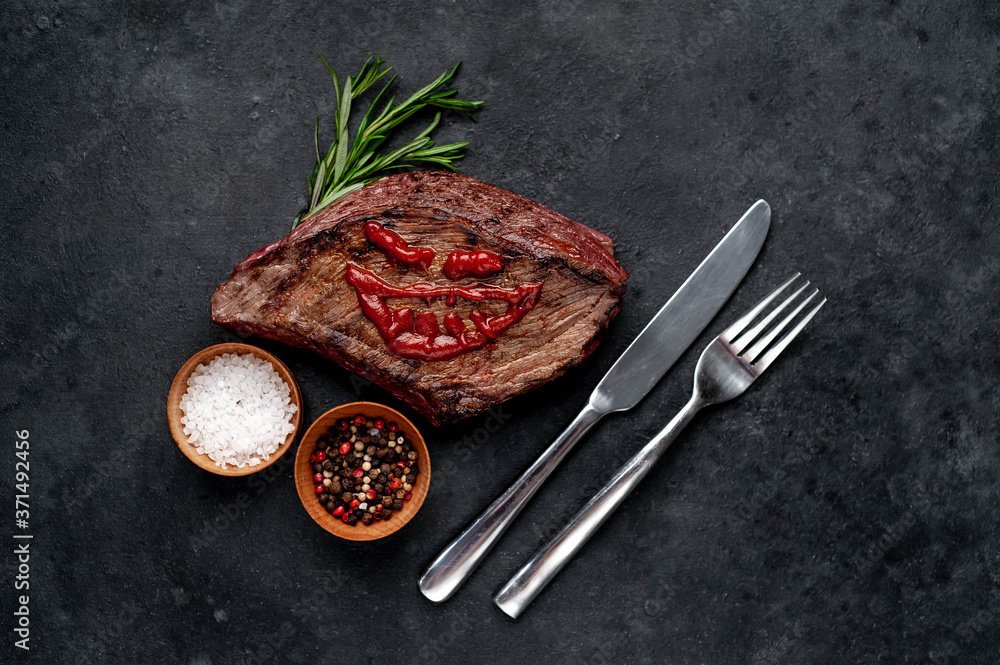grilled beef steak with spices, knife and fork for halloween on stone background grilled beef steak with spices, knife and fork for halloween on stone background