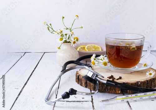 Decoction of chamomile, dried flower in flower tea and a phonendoscope, sliced lemon on a white wooden background. Health concept, prostate treatment, doctor prescribing treatment