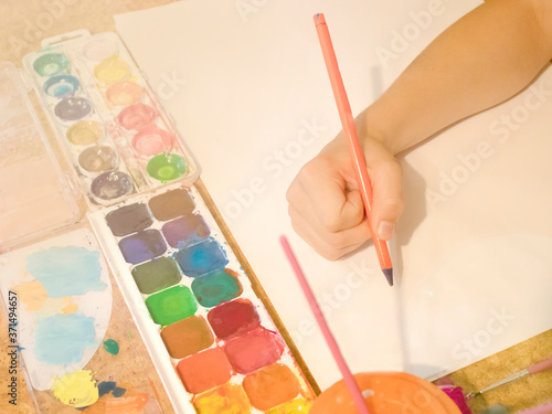 A children's hand draws on a white sheet of paper with watercolor on a bright sunny day. rippling paint and brushes. Toning is used. the concept of children's creativity
