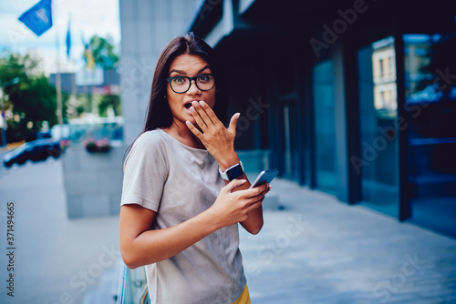 Emotional businesswoman surprised with news about startup checking email on mobile outdoors  portrait of worried female  manager in spectacles receiving message from boss spending work break outdoors