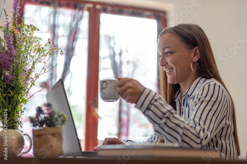 Young brunette woman drinking coffee and talking with her friend over video call.