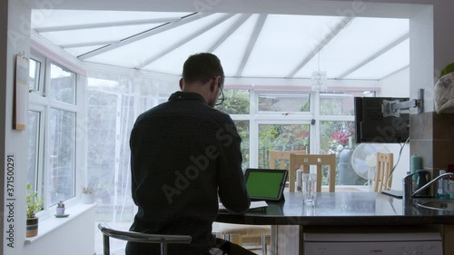 Smartly dressed man using a green screen tablet device and writing on a notepad from home wideshot