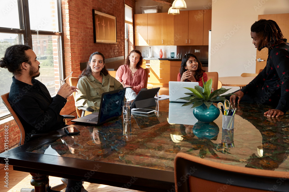 group of co-workers sitting at large conference table with their devices having discussion group of co-workers sitting at large conference table with their devices having discussion