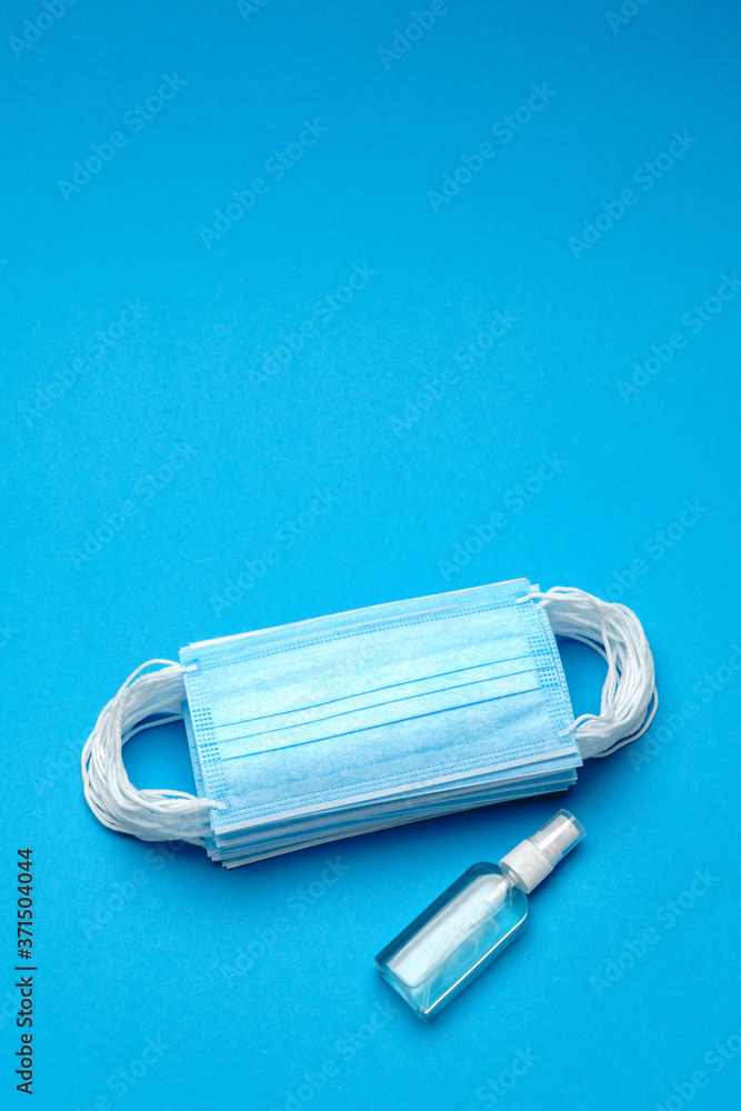 Stack of Disposable blue medical face masks and alcohol hand sanitizer antiseptic on blue background Stack of Disposable blue medical face masks and alcohol hand sanitizer antiseptic on blue background