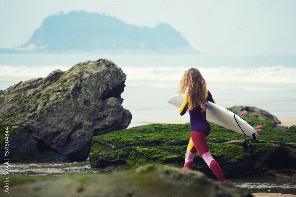 Beautiful surfer girl walking in the beach carrying her surfboard