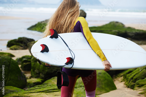 Photography Blond long-haired girl dressed in wetsuit walking to the ocean ready to surfing,
