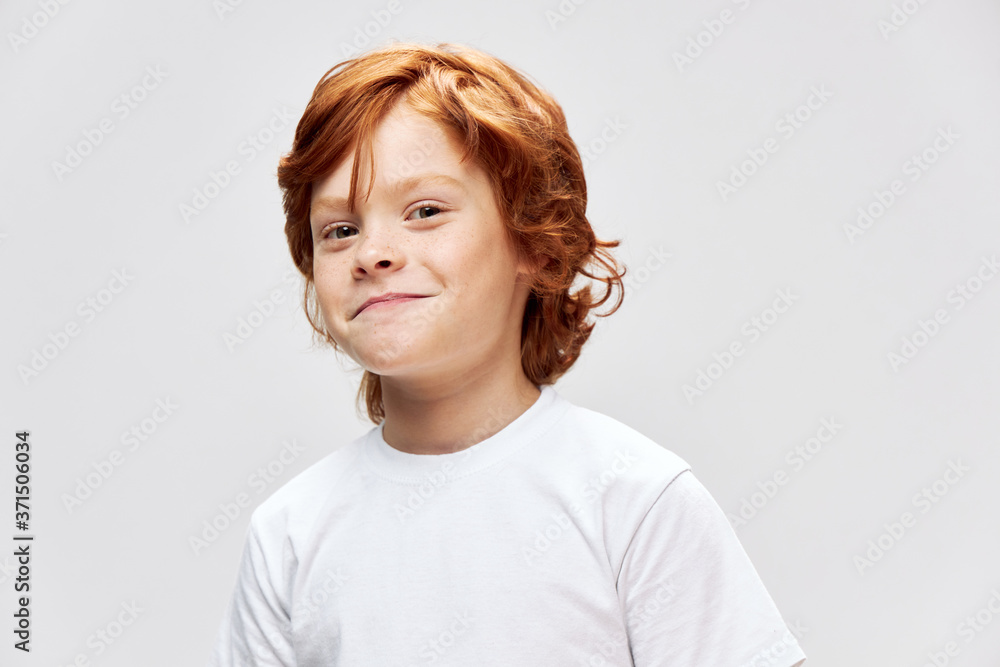 Cheerful red-haired child in a white T-shirt smile studio close-up Cheerful red-haired child in a white T-shirt smile studio close-up