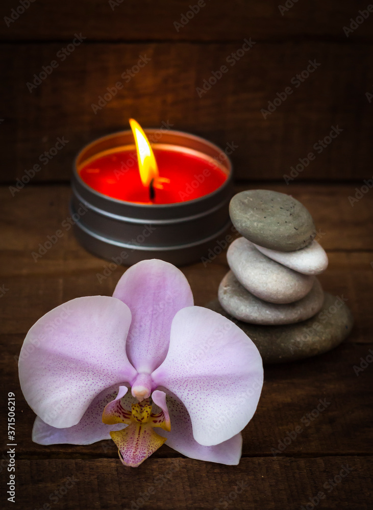 Spa stones with a pink Orchid and a burning scented candle on a brown wooden background Spa stones with a pink Orchid and a burning scented candle on a brown wooden background