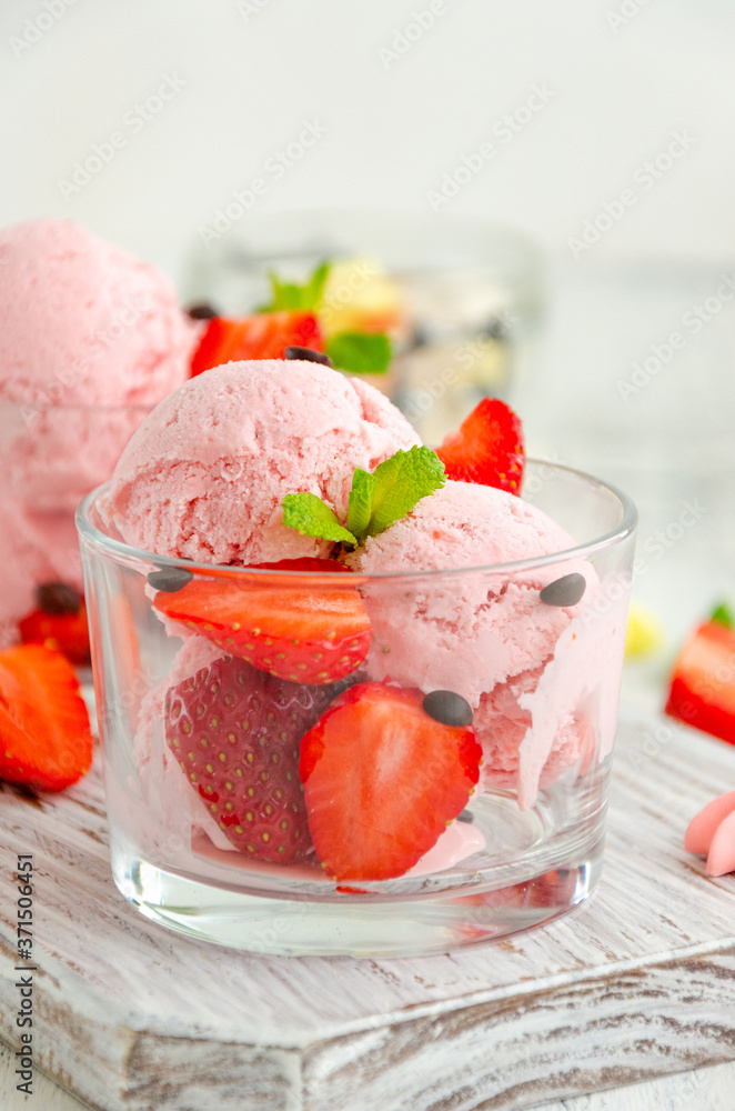 Strawberry ice cream in a glass with fresh strawberries, chocolate drops and mint on a board on a light wooden background. Vertical, copy space. Strawberry ice cream in a glass with fresh strawberries, chocolate drops and mint on a board on a light wooden background. Vertical, copy space.