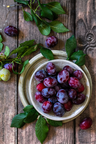 Ripe juicy plums in a bowl on a wooden background.