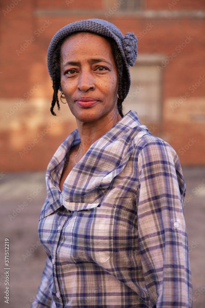 Portrait of older woman wearing knit hat standing in alley, brick wall in background Portrait of older woman wearing knit hat standing in alley, brick wall in background