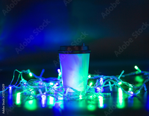 Takeaway paper cup on black background surrounded by light bulbs.