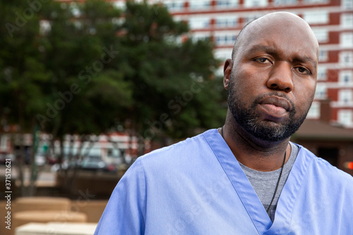 Portrait of middle aged man with beard and a bald head wearing scrubs standing outside looking at camera photo