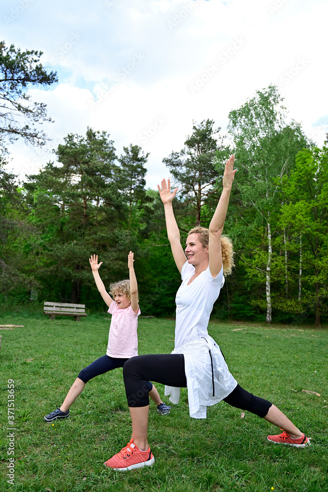 Mother with daughter practicing warrior 1 pose on grassy land in forest Mother with daughter practicing warrior 1 pose on grassy land in forest