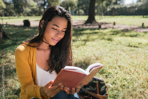 Young woman reading book while sitting on grassy land in park photo