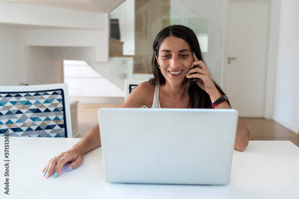 Smiling woman talking over mobile phone while using laptop on table Smiling woman talking over mobile phone while using laptop on table