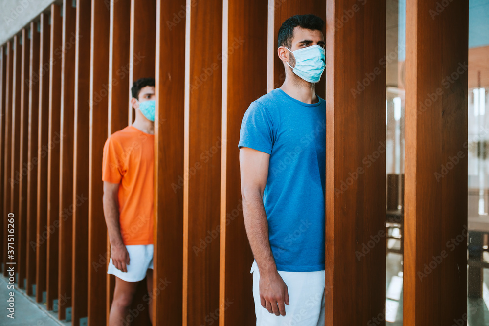 Young men wearing masks standing by wooden built structure in city Young men wearing masks standing by wooden built structure in city