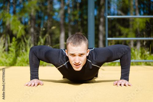 A young attractive guy does push-UPS on a sports field in the Park, training the muscles of his arms and back.