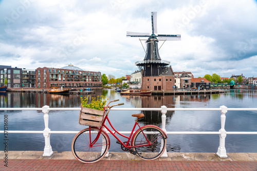 Netherlands, North Holland, Haarlem, Bicycle parked along railing of canal bridge with De Adriaan windmill in background photo