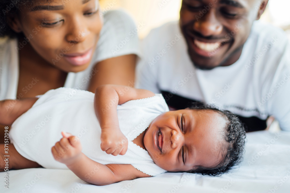 © Westend61 - Close-up of smiling parents looking at newborn daughter sleeping on bed