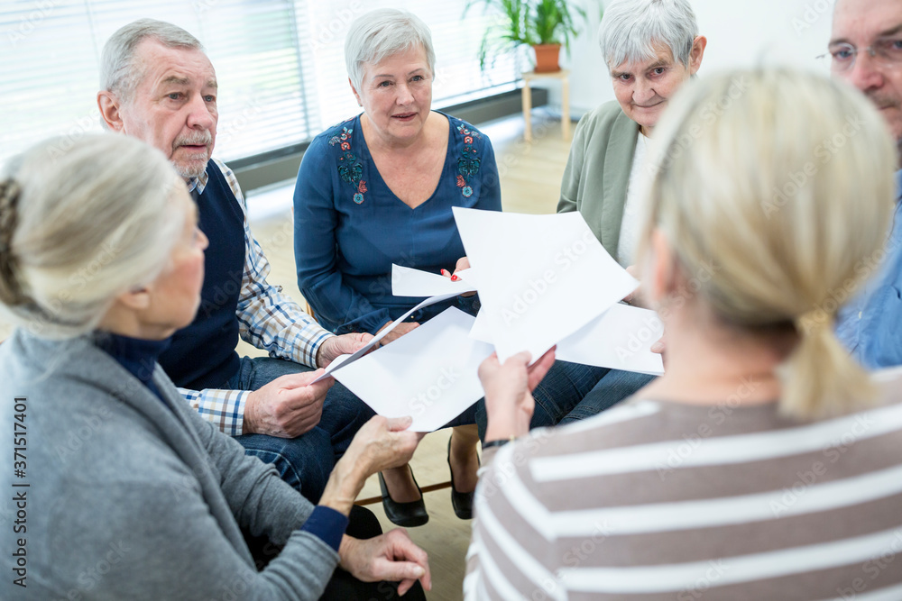 Group of seniors attending therapy group in retirement home, using sheets of paper Group of seniors attending therapy group in retirement home, using sheets of paper