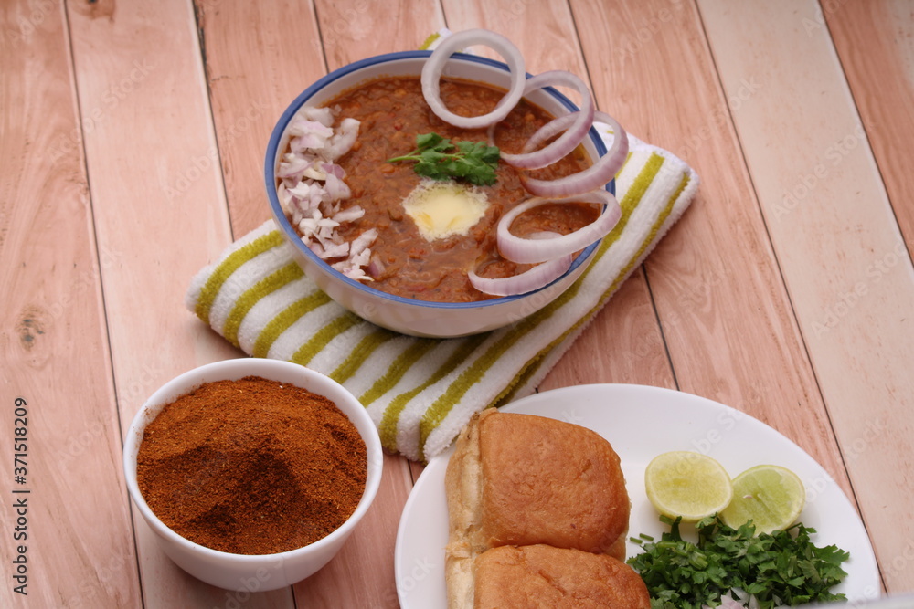 Pav Bhaji, it is Thick and spicy vegetable curry and served with a soft bread and butter. With pavbhaji masala on wooden background.