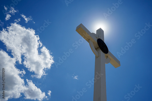 white chrestian cross on a background of blue sky, white clouds and sunbeams photo