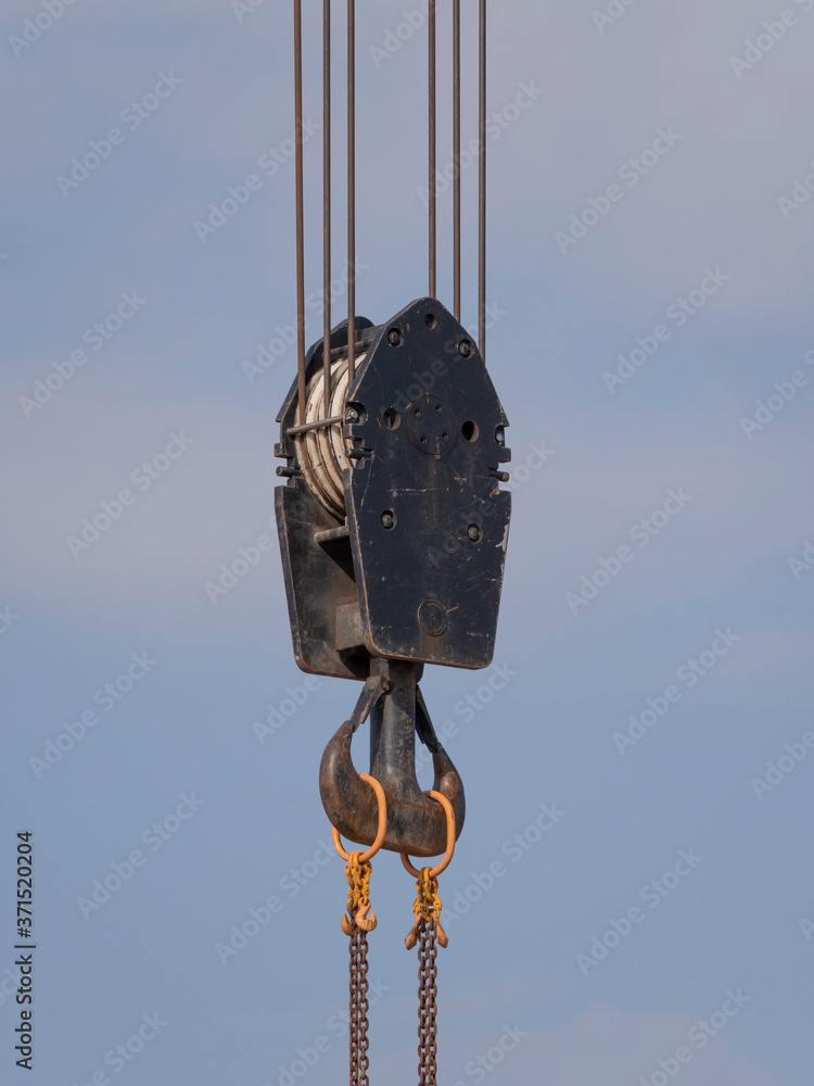 Crane hook with red and white stripes hanging, blue sky in background Crane hook with red and white stripes hanging, blue sky in background