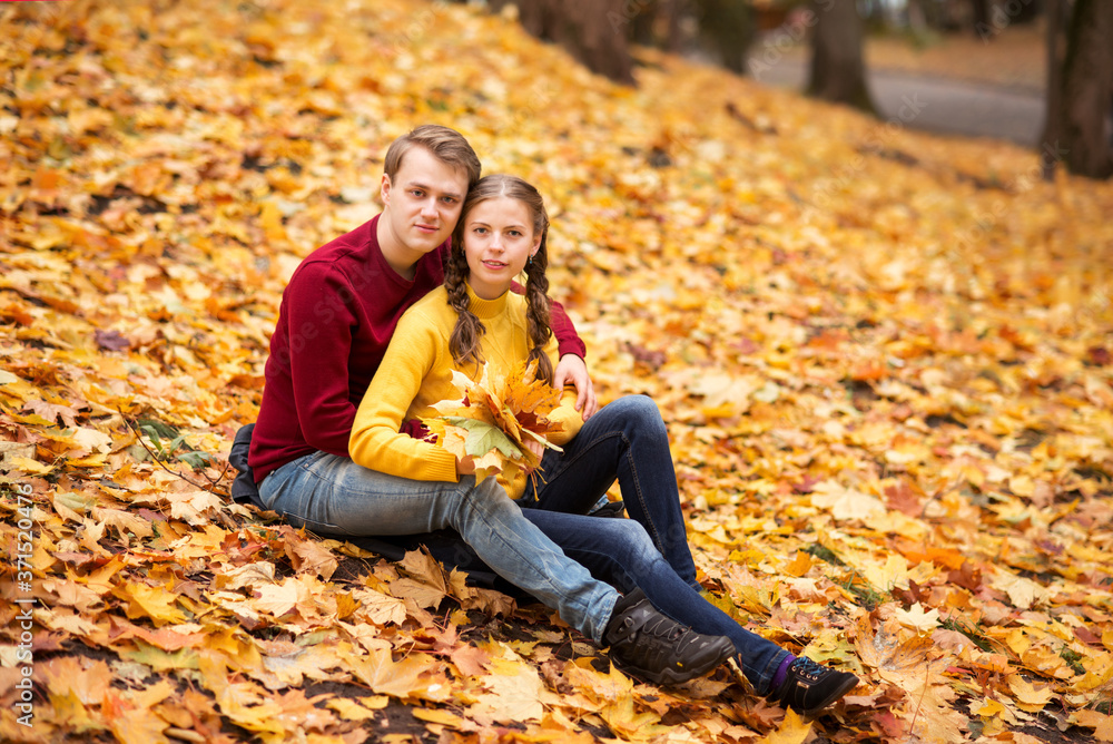young couple sits on yellow autumn leaves in a Park. Bouquet of autumn leaves young couple sits on yellow autumn leaves in a Park. Bouquet of autumn leaves