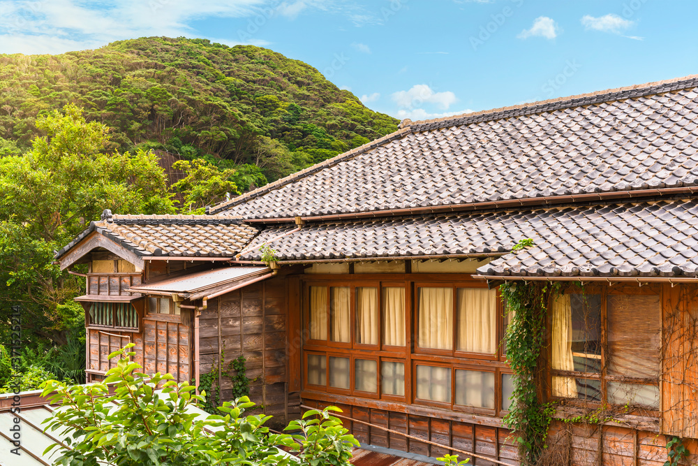 Traditional japanese Yosemunezukuri hip roof and sasarako-shitami wooden facade covered with climbing plants on the Kajiya ryokan guesthouse at the foot of Mount Nokogiri.