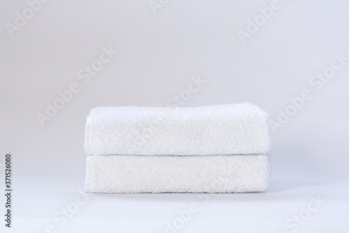 Two white neatly folded terry towels on a light background.